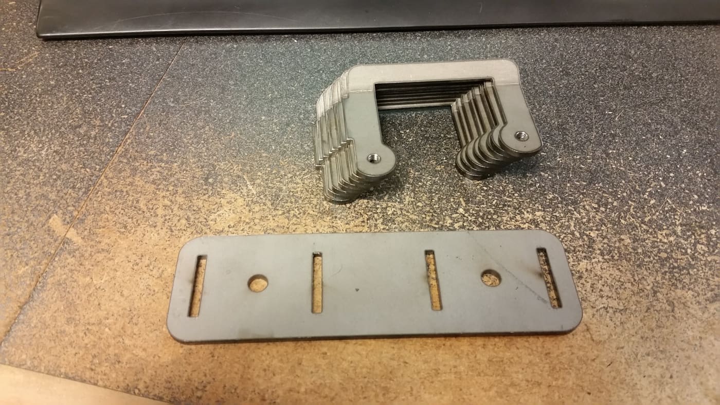 Formed aluminium handle bracket beside a laser-cut slotted flat plate